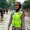 Seorang petugas mengatur lalu lintas yang terendam banjir