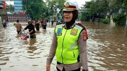 Seorang petugas mengatur lalu lintas yang terendam banjir