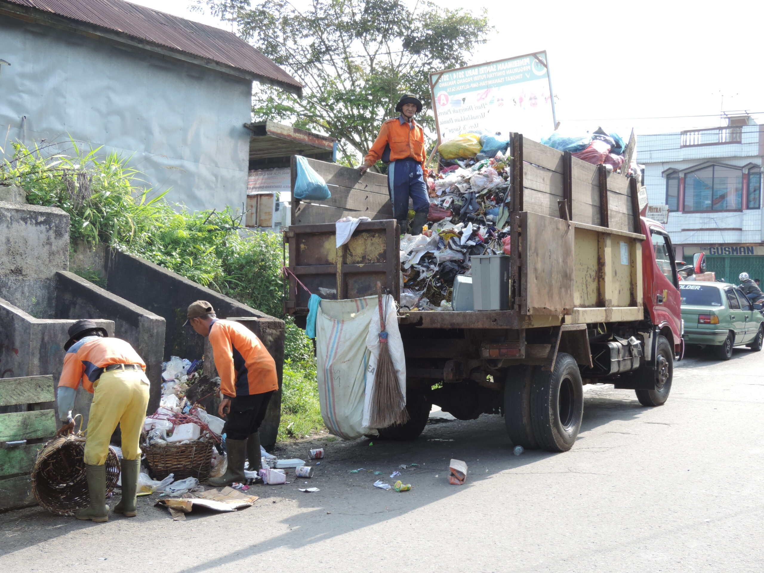 Pekerja kebersihan pada truk sampah sedang mengambil sampah di tepi jalan raya untuk dibuang ke TPA Sampah Sungai Andok.